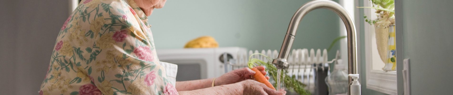 Une femme âgée prépare de la nourriture dans la cuisine.