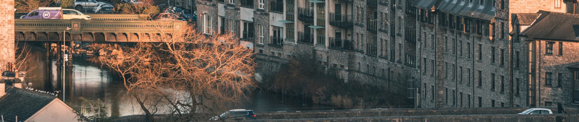 Vue urbaine d'un pont en pierre au-dessus d'une rivière entourée de maisons.