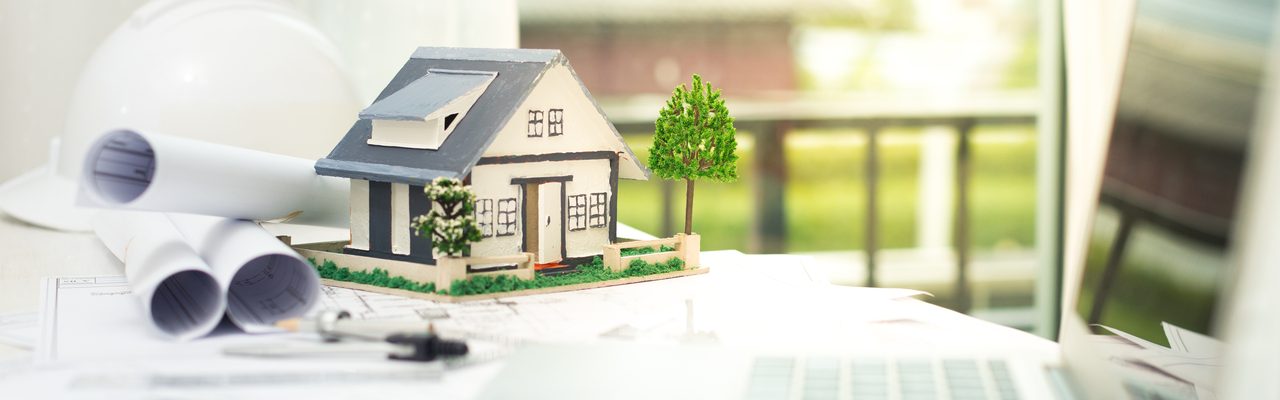 Un ordinateur portable et un modèle de maison posés sur un bureau.