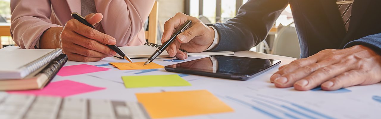 Deux personnes assises à une table, tenant un crayon, écrivent sur un post-it.